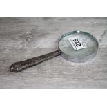 Silver handled magnifying glass, the handle with repousse floral and foliate scroll decoration,