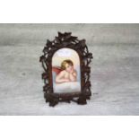 19th century Black Forest Carved Wooden Frame with Hand Painted Ceramic Panel depicting a Cherub