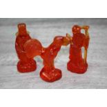 Three resin amber Oriental coloured figurines, modelled as a an Elder with staff, a robed Elder