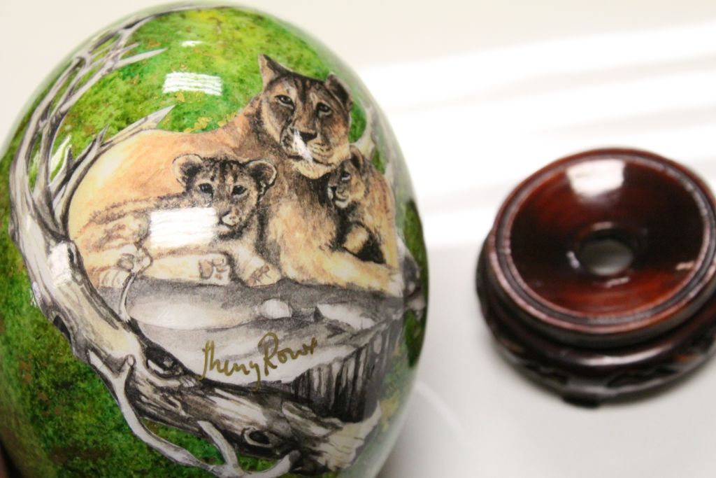 Hand painted signed ostrich egg on carved hardwood stand, green and gilt ground depicting lioness - Image 2 of 2