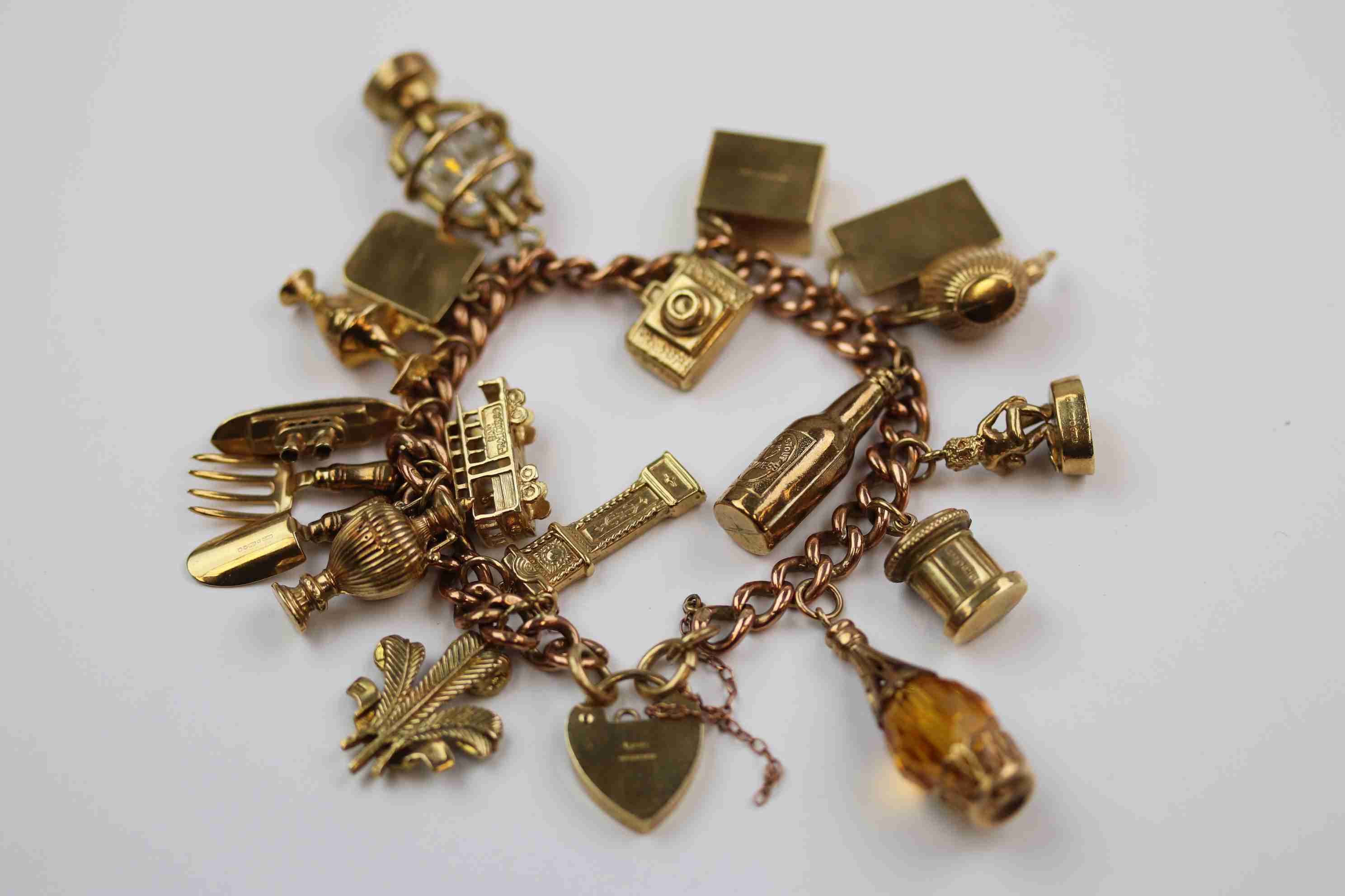 9ct rose gold curb link charm bracelet with 9ct yellow gold padlock clasp, seventeen charms in total