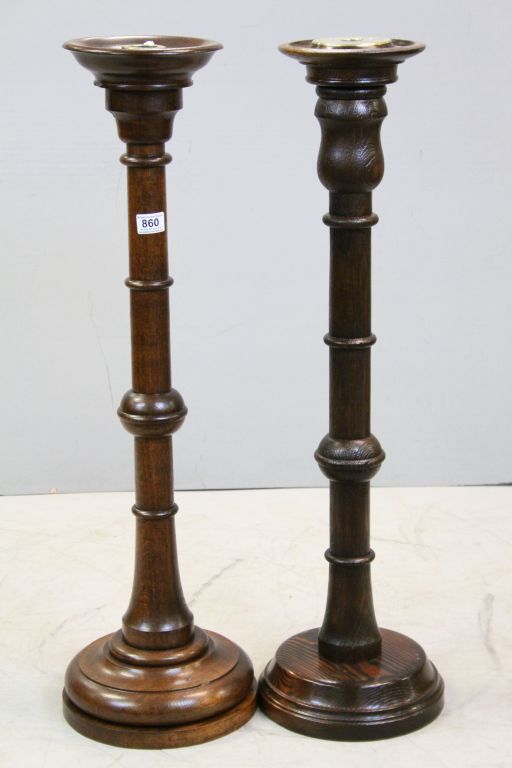 Two similar Oak Standard Candle Stands each set with a Brass Candle Holders and raised on turned