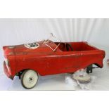 Vintage red pedal car in red, in need of repair, rusted and play worn with one loose wheel, mid 20th