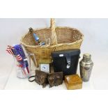 A wicker basket containing a mixed lot of collectables to include binoculars, cocktail shaker and