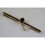 Garnet unmarked gold bar brooch, the central oval mixed cut garnet measuring approximately 6mm x