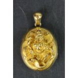 Yellow metal oval locket with repousse Indian style figural decoration, glazed panel to interior,
