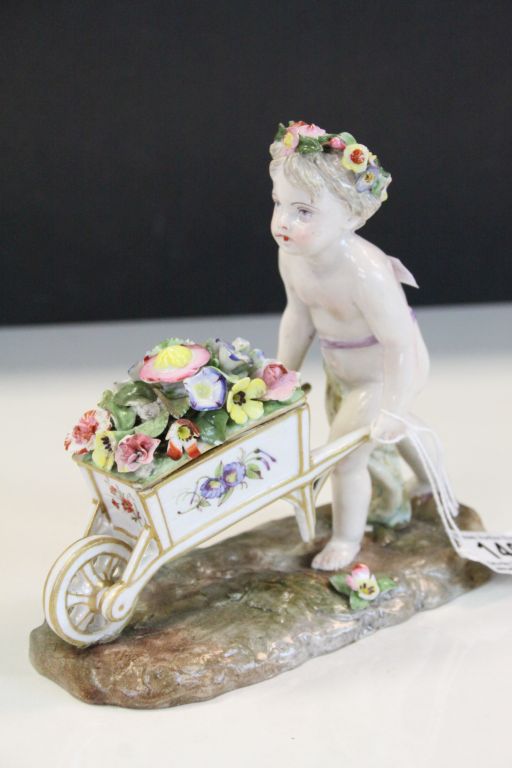 Meissen style ceramic figurine of a Garland Flower wearing Cherub pushing a wheelbarrow of Flowers