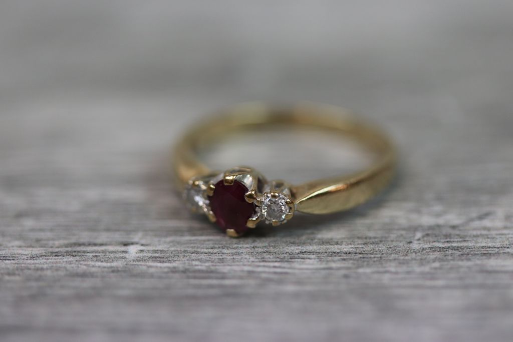 Ruby and diamond three stone 9ct yellow gold ring, the central oval mixed cut ruby measuring