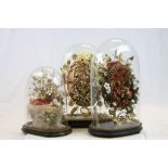 Three Victorian Glass dome covered Floral style displays in Wax, Ceramic, velvet cushion etc,