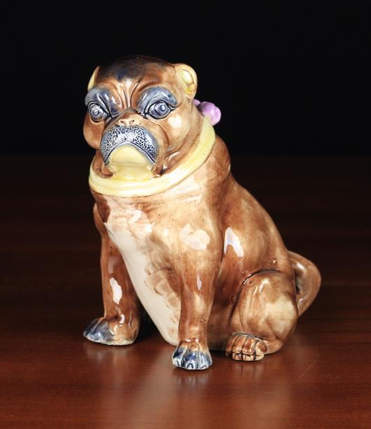 A 19th Century Majolica Pug Dog modelled seated wearing a yellow collar with pink bow & bells.