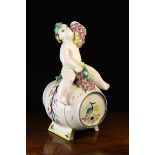 A Faience Barrel straddled by the figure of a bacchanalian putto wreathed in vine,