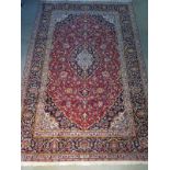 A hand knotted woollen kashan rug with red ground and blue borders, approx 212cm x 138cm, in good