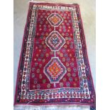 A hand knotted woollen rug with a red field, some wear, small hole - 206cm x 110cm