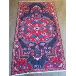 A hand knotted woollen rug with a red field, generally good, some small wear - 204cm x 112cm