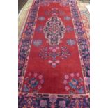 A hand knotted red ground woollen rug, approx 314cm x 146cm, with some colour bleeding