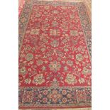 A machine made woollen rug with a red field - 310cm x 200cm - some usage wear mainly to edges,