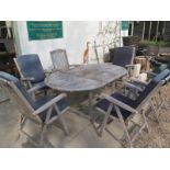 A good quality weathered teak oval extending garden table with six folding chairs and cushions