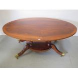 A modern mahogany veneered oval coffee table on four outswept legs with brass casters - 142cm long x