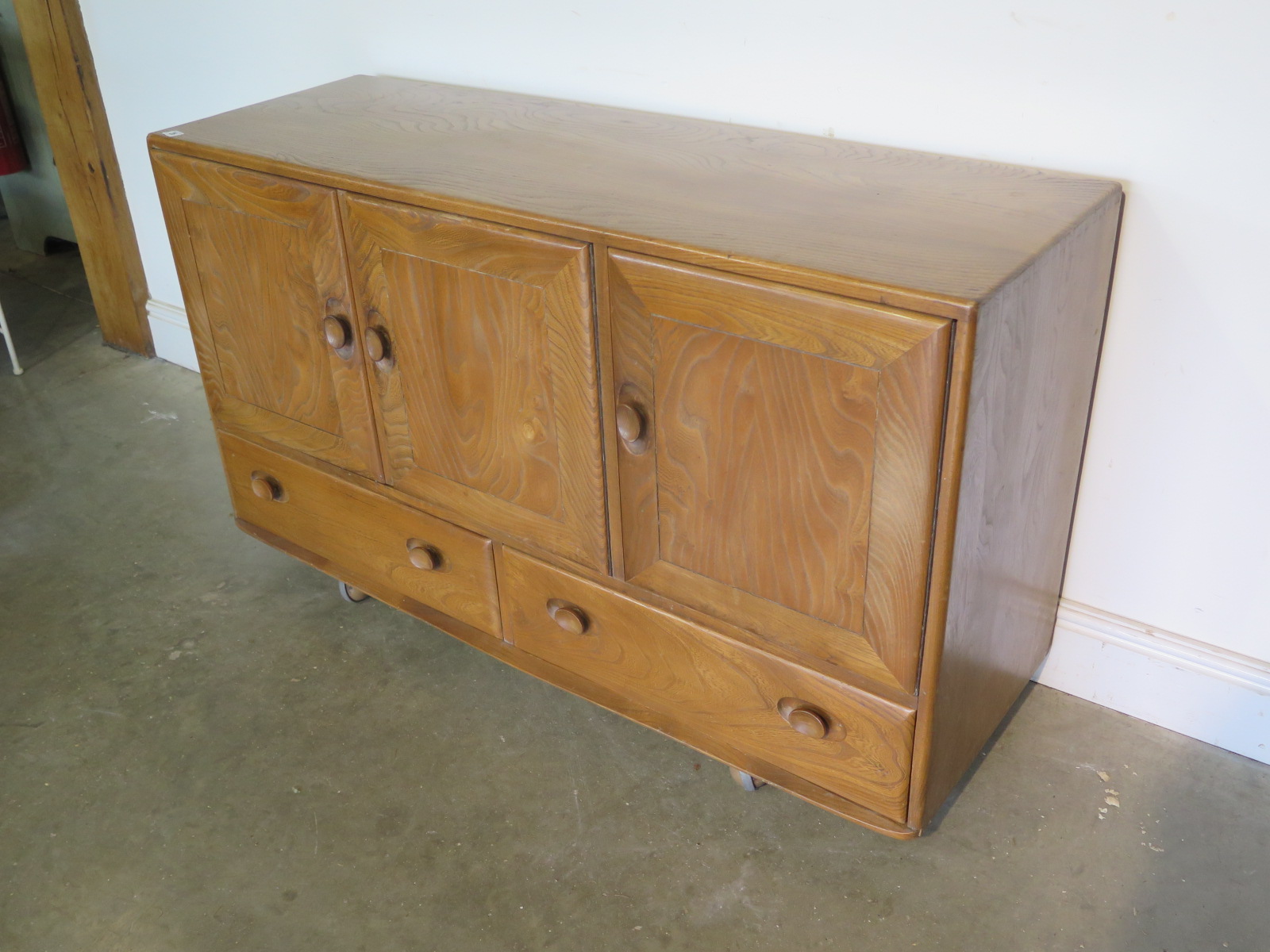 An Ercol blonde elm and beech sideboard with three cupboard doors over three drawers, missing its - Image 3 of 4