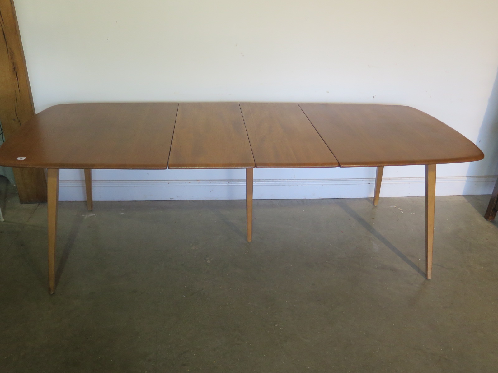 An Ercol blonde elm and beech extending table with a folding two section leaf raised on five