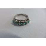 A white metal half hoop ring set with five emeralds, size L, the 3-4mm facetted pale emeralds are