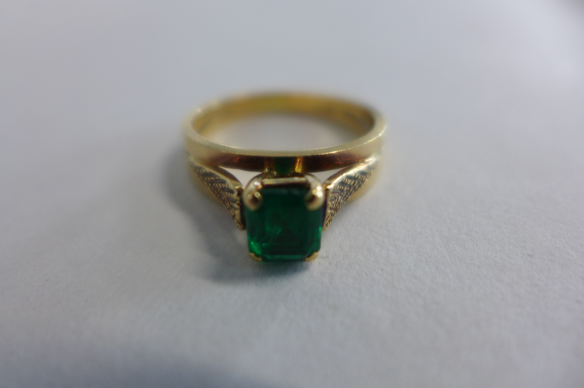 Yellow metal emerald dress ring, the step cut emerald is held by four corner claws and measures