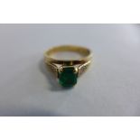 Yellow metal emerald dress ring, the step cut emerald is held by four corner claws and measures