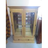 A glazed two door display cabinet, with base drawer, 139cm tall x 93cm x 48cm