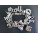A heavy silver charm bracelet with approx 28 different charms including encased £1 note - approx