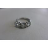 A platinum three stone diamond ring, the central oval diamond 0.64 carat, flanked either side by