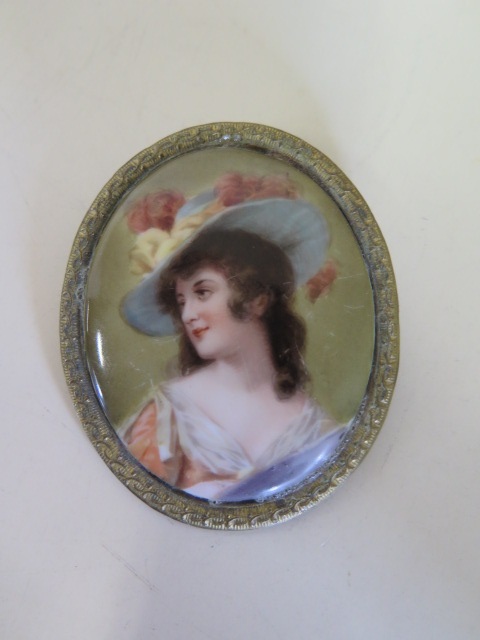 A hand painted porcelain plaque brooch of an attractive lady wearing a hat, 7x6cm, some scratches