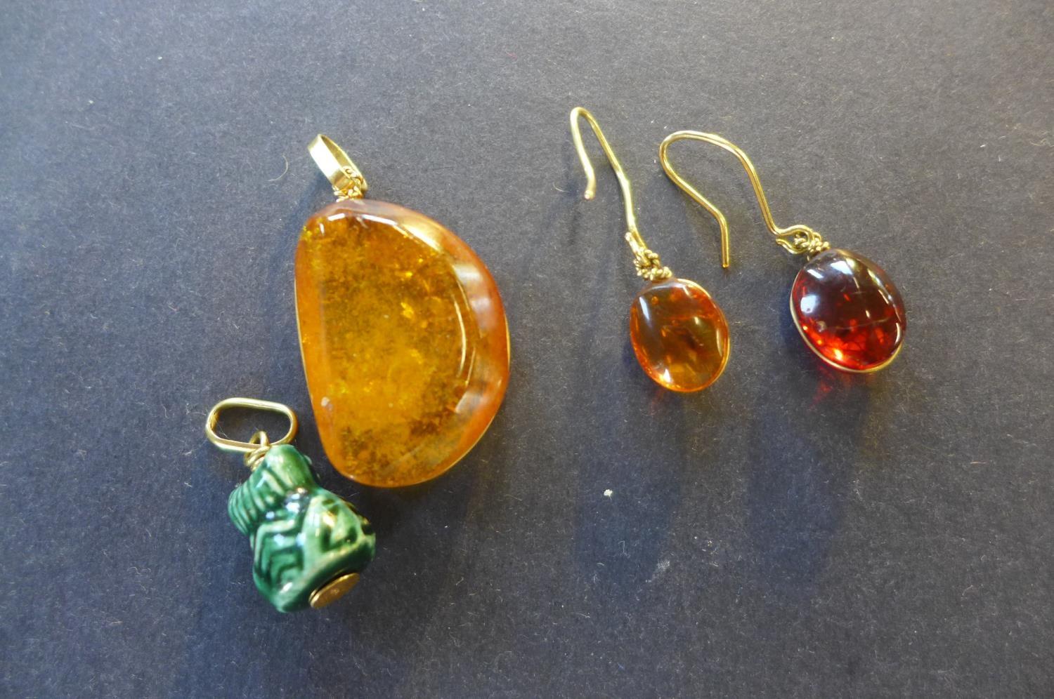 A polished amber pendant, measuring 30mm x 20mm x 9mm with yellow metal mount and pair of similar