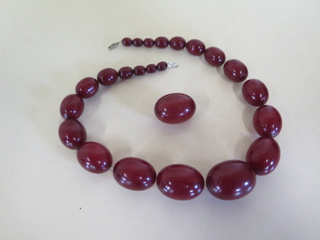 A string of cherry amber Bakelite beads, length 50cm, largest bead length 37mm, also a loose bead,