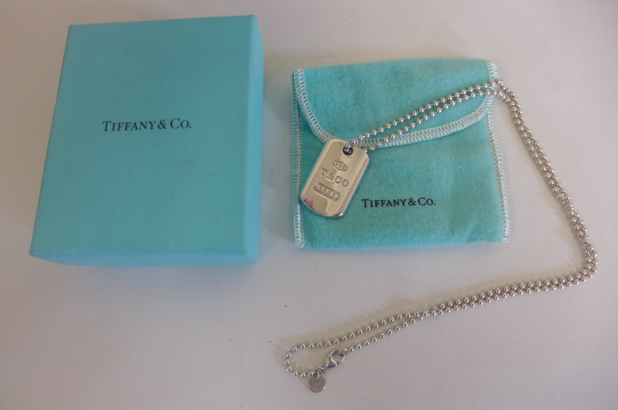 A Tiffany and Co silver dog tag on chain, with box and pouch, some minor scratches but reasonably