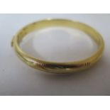 A yellow metal hollow hinged D profile bangle, engraved pattern throughout to a push clasp with