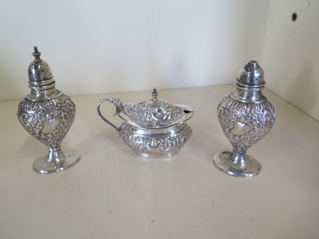 A silver embossed three piece cruet set, hallmarked Birmingham 1909 - by Joseph Glostor Ltd,