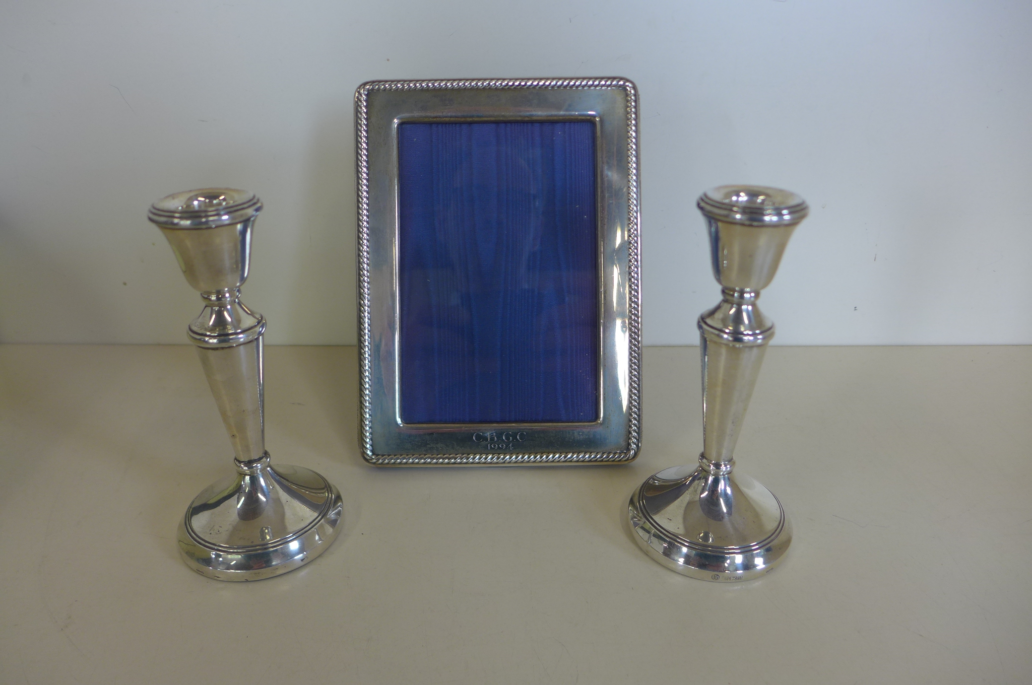 A pair of weighted silver candle sticks, 15cm tall, and a silver photo frame, 19x14cm, both