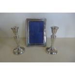 A pair of weighted silver candle sticks, 15cm tall, and a silver photo frame, 19x14cm, both