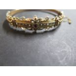 An Edwardian 9ct yellow gold bangle, push clasp with scrolled design and beading, set with a