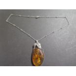 A large polished amber pendant, silver set with a stylised leaf surmount and bezel, amber approx