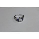 A diamond and sapphire trilogy ring with diamond set shoulders set in 18ct white gold, ring size