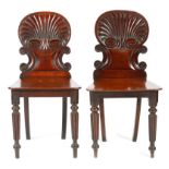 A near pair of Regency mahogany hall chairs in the manner of Gillows, each with a scroll and shell