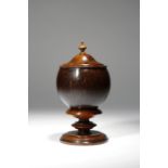 An early 19th century coconut and treen cup and cover, the lid with a turned urn finial, on a turned