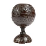 A carved coconut cup, naively carved in relief with natives in various pursuits: climbing palm