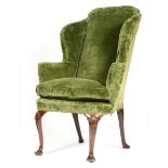 A George II red walnut wing armchair, later upholstered with green plush fabric, on shell and husk