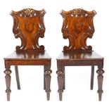 A pair of Victorian oak hall chairs, each with a scroll carved back, centred with a vacant shield,