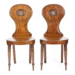 A pair of Regency mahogany hall chairs, each with a reeded oval back carved with a shell, above a