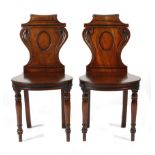 A pair of Regency mahogany and ebonised hall chairs, each with a scroll top rail above a waisted