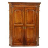 A mid-18th century elm and oak hanging corner cupboard, with a pair of fielded panel doors enclosing