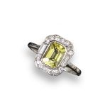 A yellow sapphire and diamond cluster ring, the emerald-cut sapphire is set within a surround of